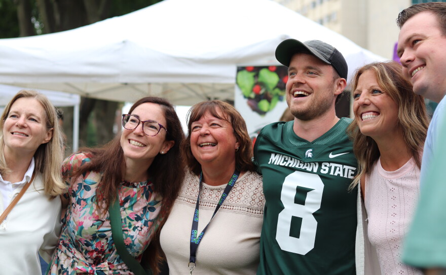 Photos of Josh and Jace, two young British men, taking photos with fans and mascots. The two are wearing a blue University of Michigan and a green Michigan State University jersey respectively.