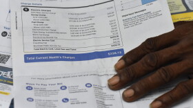 An up-close photo of a Tampa Electric Power bill shows charges totaling $338 with a man’s hand resting on the bottom of the page.