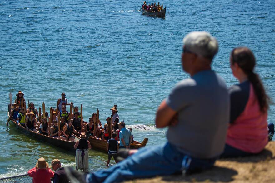 People watch canoes welcomed onto dry land.