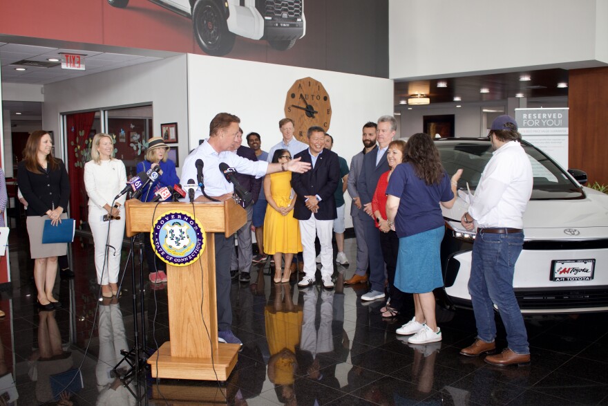 Governor Ned Lamont, legislators, and advocates admire an electric car at A-1 Toyota in New Haven.