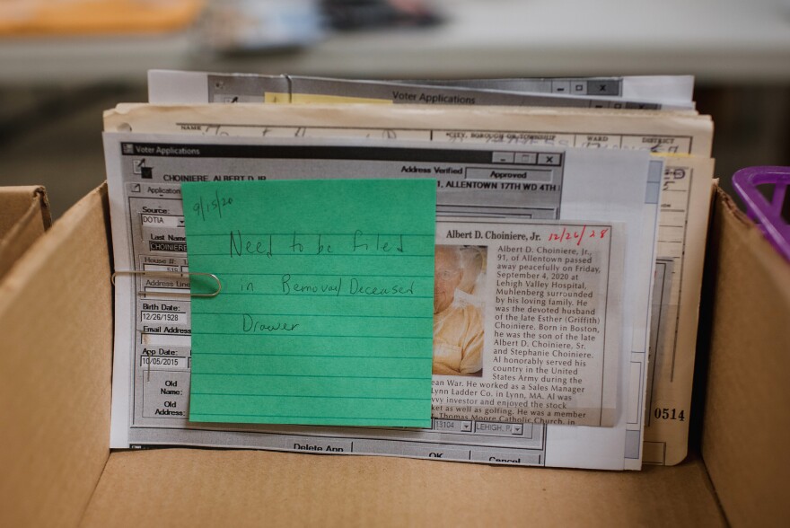 A memo stating "Need to be filed in Removal/Deceased Drawer" is attached to an obituary newspaper clipping. Election workers check obituaries to make sure ballots are not sent to people who have died.