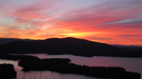The run rising over Squam Lake with yellow, orange, pink and purple hues.
