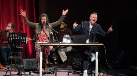 Two podcast hosts on the stage in front of their microphones. 