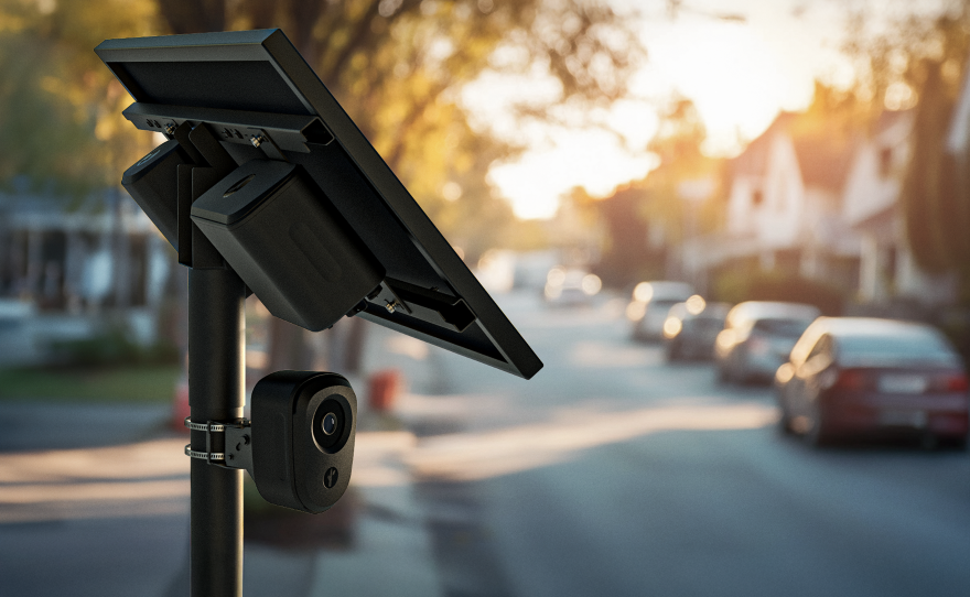 a black, pole-mounted camera on a residential street with a solar power panel