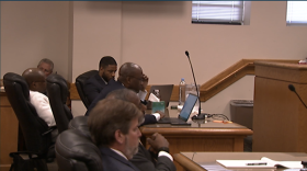 The defense and prosecution sit at their respective tables in a courtroom listening to testimony played back for the jurors.