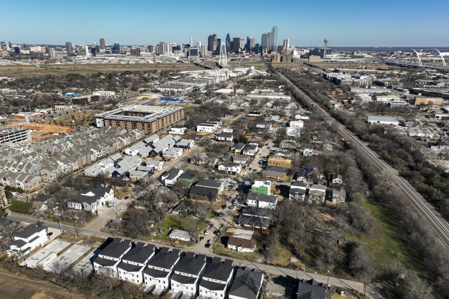 An aerial view of the neighborhood in the foreground with the downtown Dallas skyline in the background.