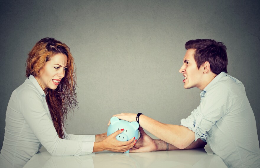 Finances in divorce concept. Wife and husband cannot make a settlement, and they're holding a piggy bank sitting at table looking at each other with hatred.