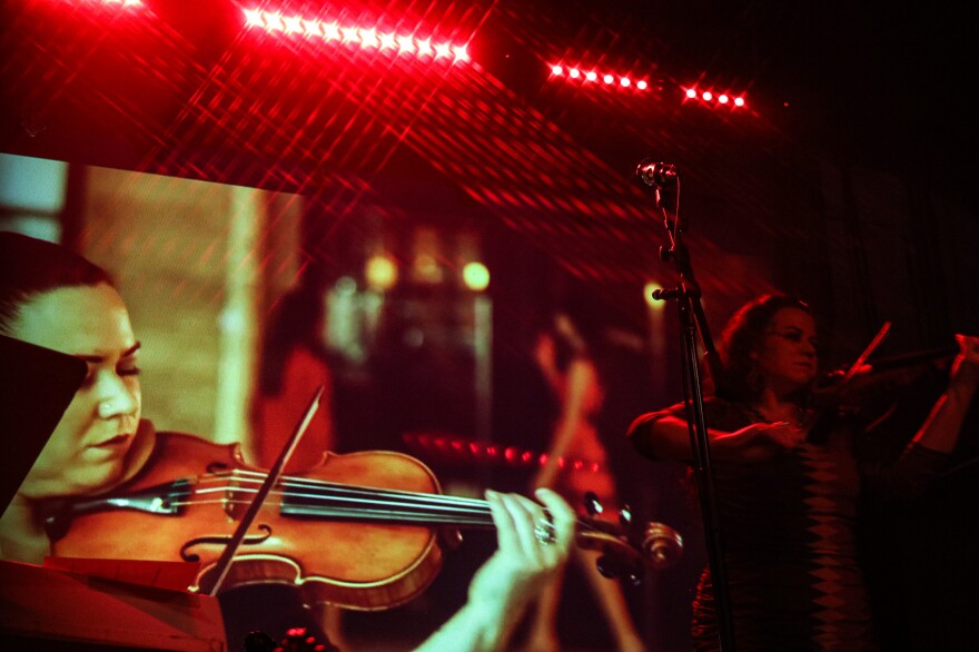 A female violinist performs in front of a video of herself doing the same.