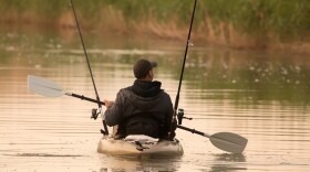 A man use an oar in his kayak with two fishing rods sticking up