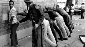 FILE - In this July 24, 1967 file photo, a Michigan State police officer searches a youth on Detroit's 12th Street where looting was still in progress after the previous day's rioting. The last surviving member of the Kerner Commission says he remains haunted that the panel's recommendations on US race relation and poverty were never adopted, but he is hopeful they will be one day. Former U.S. Sen. Fred Harris says 50 years after working on a report to examine the causes of the late 1960s race riots he strongly feels that poverty and structural racism still enflames racial tensions even as the United States becomes more diverse. (AP Photo/File)