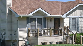 A light-colored, wood-frame house sits with some black graffiti on the left side and two windows near the front porch showing evidence of egg splatters.