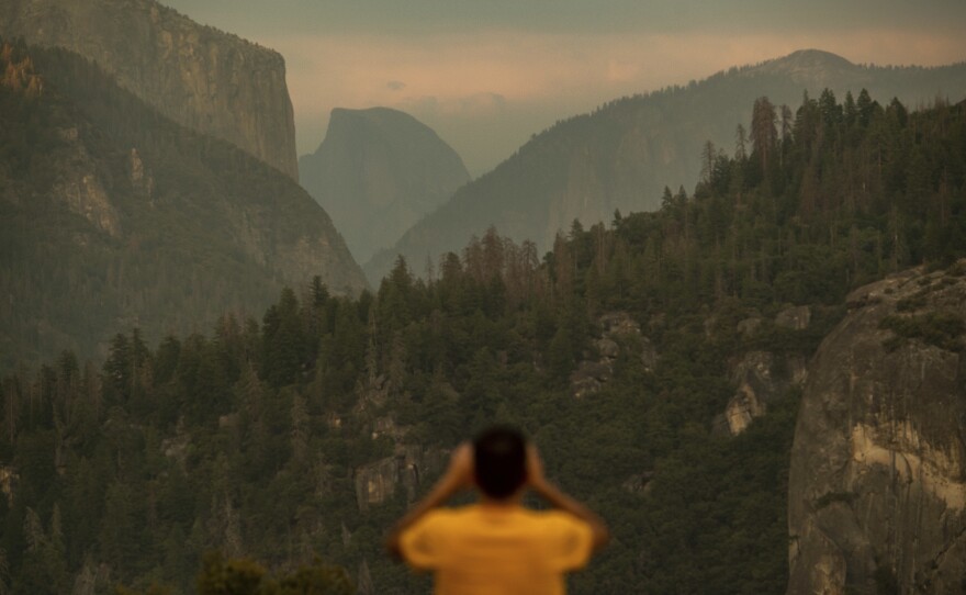 A visitor photographs Half Dome on Tuesday as smoke from the Ferguson Fire is visible in Yosemite National Park, a day before authorities closed parts of it.