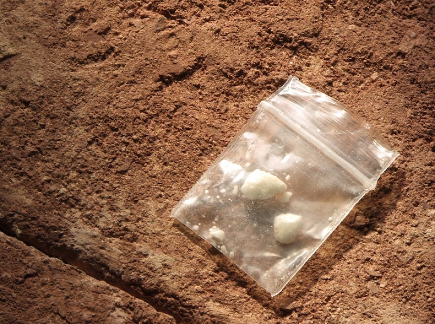 A photo showing a small plastic baggie with white powdery substance clumped in two balls, against dirt in the background.