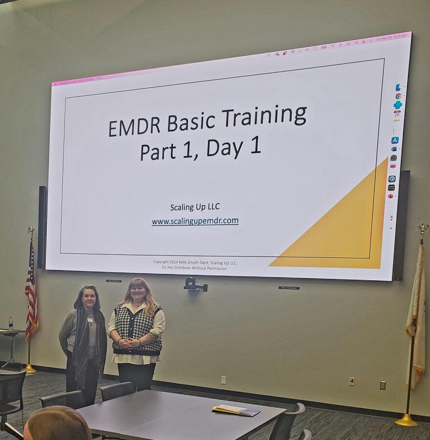 A picture of two women standing in front of a big display screen. Barbara Sheehan-Zeidler of Scaling UP LLC [left] and Samantha Herrell, McLean County Behavioral Health Coordination [right] start a multi-day training for social workers and therapists in EMDR, held recently at Heartland Community College.