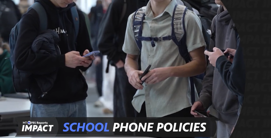 Screen capture from “Montana PBS Reports: IMPACT” showing several high school students standing in a hallway, each looking down at and using a smartphone. The students wear backpacks and casual clothing. A banner at the bottom reads “IMPACT” and “School Phone Policies.”
