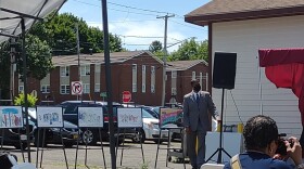 A man in a gray suit stands to the side of five different art pieces that all have brick backgrounds. 