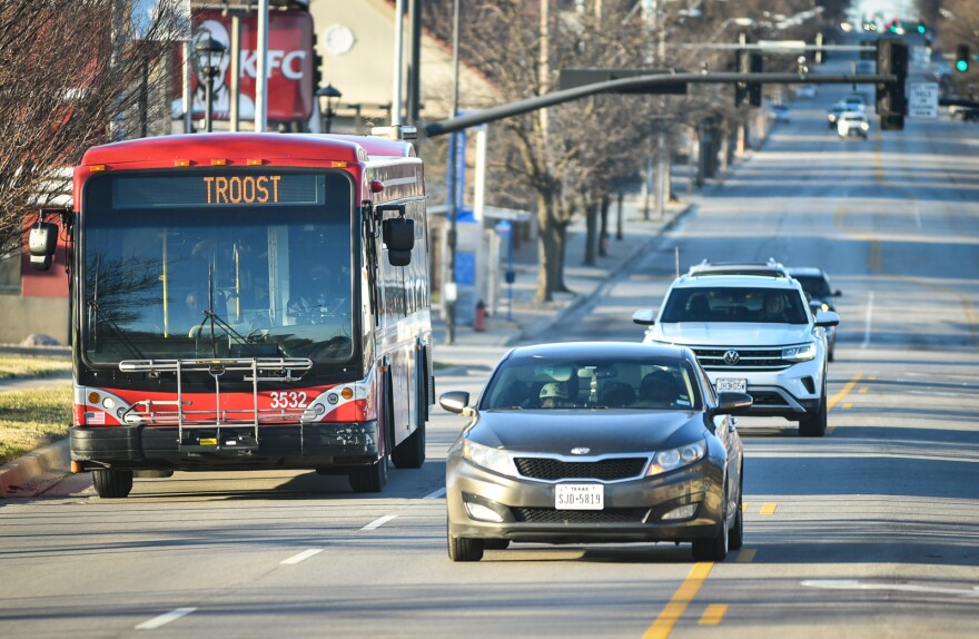 A red commuter bus rides in the left lane of a street with other car traffic moving alongside of it.