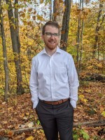 Nicholas Booker in dress clothes in a forest during the autumn