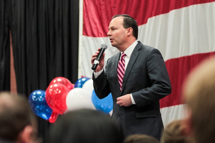 Senator Mike Lee speaks into a microphone in front of american flag and balloons.