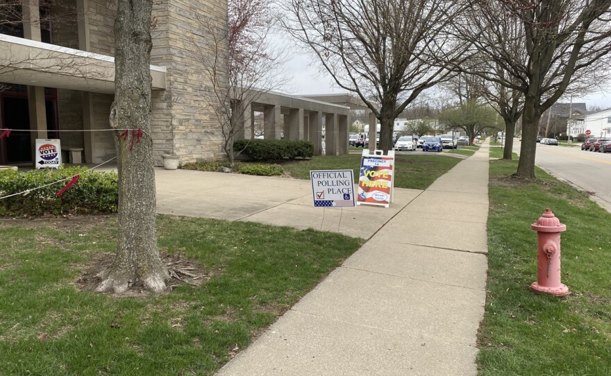 Sidewalk entrance to a church that includes a sign with wording 'Official Polling Place' and a sandwich board with an image of an American flag and the words 'Vote Here' on the side.
