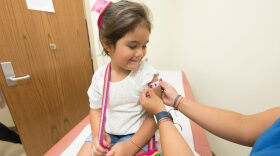 A health care worker places a bandage on a child after giving a vaccination shot. New federal guidance to reduce the number of recommended childhood vaccines from 17 to 11 comes as states including Florida are already charting their own course on vaccine policy.