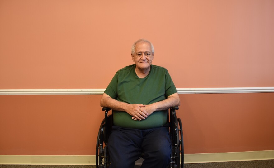 phil in a wheelchair wears a green shirt and sitting in front of a peach colored wall