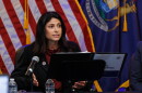 Attorney General Dana Nessel sits in front of United States and Michigan state flags and reads from a folder placed on a stand in front her.