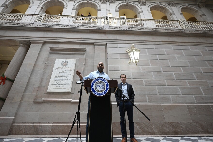 Mayor Elect Arunan Arulampalam addressing the mayoral transition with current Hartford Mayor Luke Bronin. Two individuals listen in from above as Arulampalam’s voice projects through the halls of City Hall. Hartford, Connecticut. December 29, 2023.