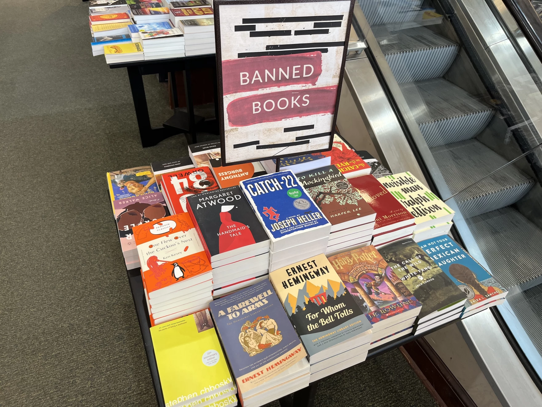 A table in an Iowa bookstore displaying Banned Books. Among the titles are The Handmaid's Tale, A Farewell To Arms, Invisible Man, Catch-22, and many more.