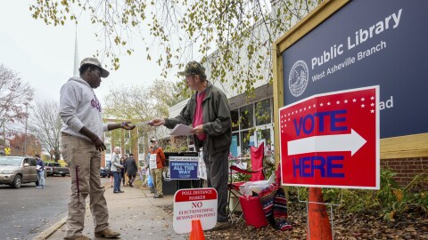 Stephen McCutcheon, right, gives a sample Republican ballot to Douglas Frick outside the West Asheville Public Library on Election Day, Tuesday, Nov. 5, 2024 in Asheville, N.C.