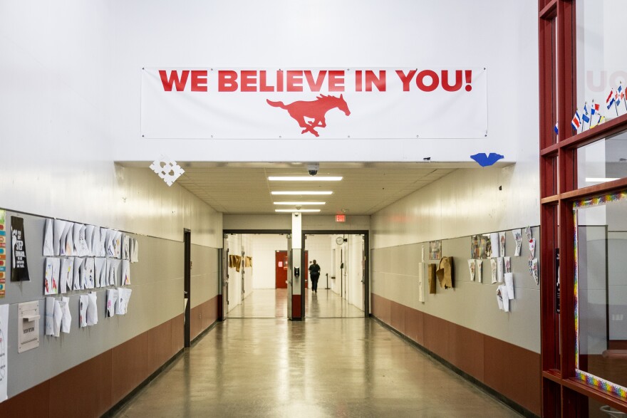A sign with an icon of a racing horse says, We believe in you! It's hanging above a school hallway.