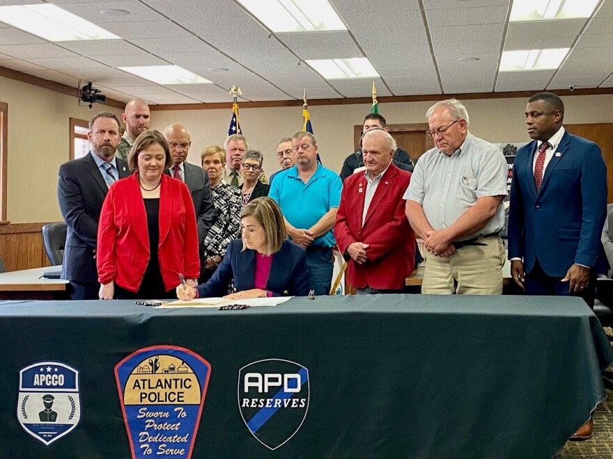 governor kim reynolds signs a bill into law surrounded by law enforcement officials and lawmakers