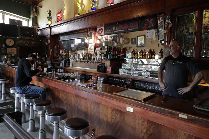 A man sits and eats at a bar as a bartender stands behind it. 