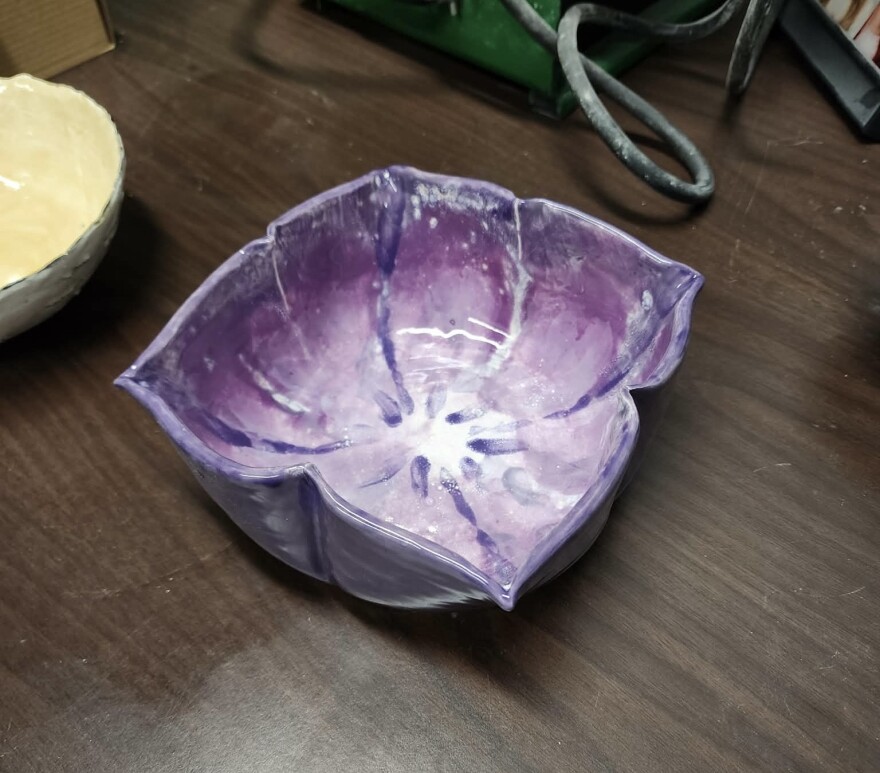 A ceramic bowl int he shape of a purple flower on a wooden table.