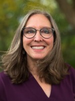 A picture of a white woman in a purple shirt with glasses