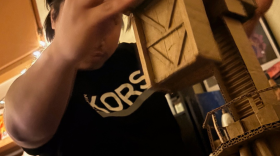 Jeimax Ruloma working on The Crane. Ruloma constructs industrial machines from fragile cardboard materials, exploring the precarious nature of capitalist systems and the tension between strength, labor, and impermanence.