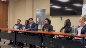 Attorney Shiraz Khan sits by Clark's mother to his right and Clark's son to his left. Large promotional posters from the Shiraz Law Firm bearing the headline "Press Release: Justice for Krystal Clark" stand in the background.