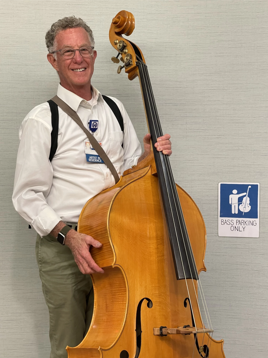 Un hombre sosteniendo un contrabajista, vestido con una camisa blanca and puesto anteojos