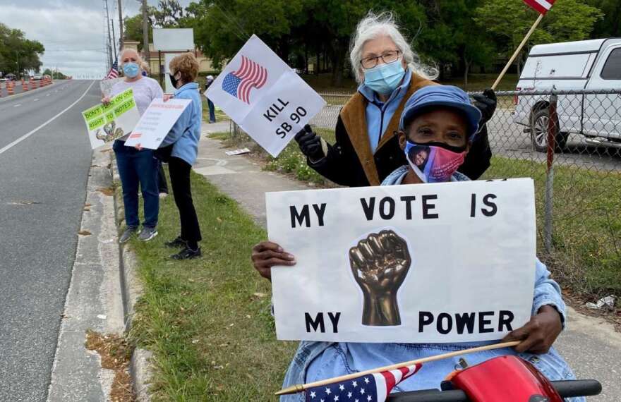 Regina Sapp in her wheelchair and Ava Barnes protest against Sen. Dennis Baxley's elections bill on Saturday in Lady Lake. A House bill on the issue was debated in Tallahassee on Monday. Photo: Joe Byrnes, WMFE