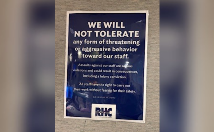 A blue sign with white lettering that is taped to a wall warns against threatening or aggressive behavior toward staff.