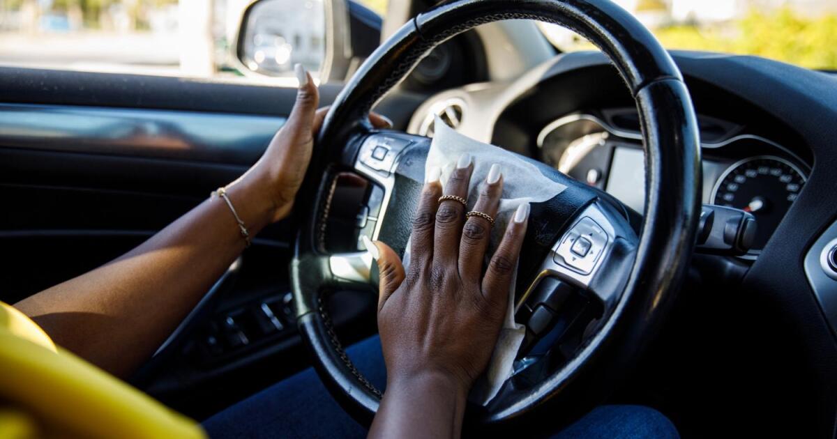 A woman cleans her car's steering wheel with a wet wipe