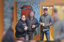 Three people stand in front of a painting holding coffee mugs.