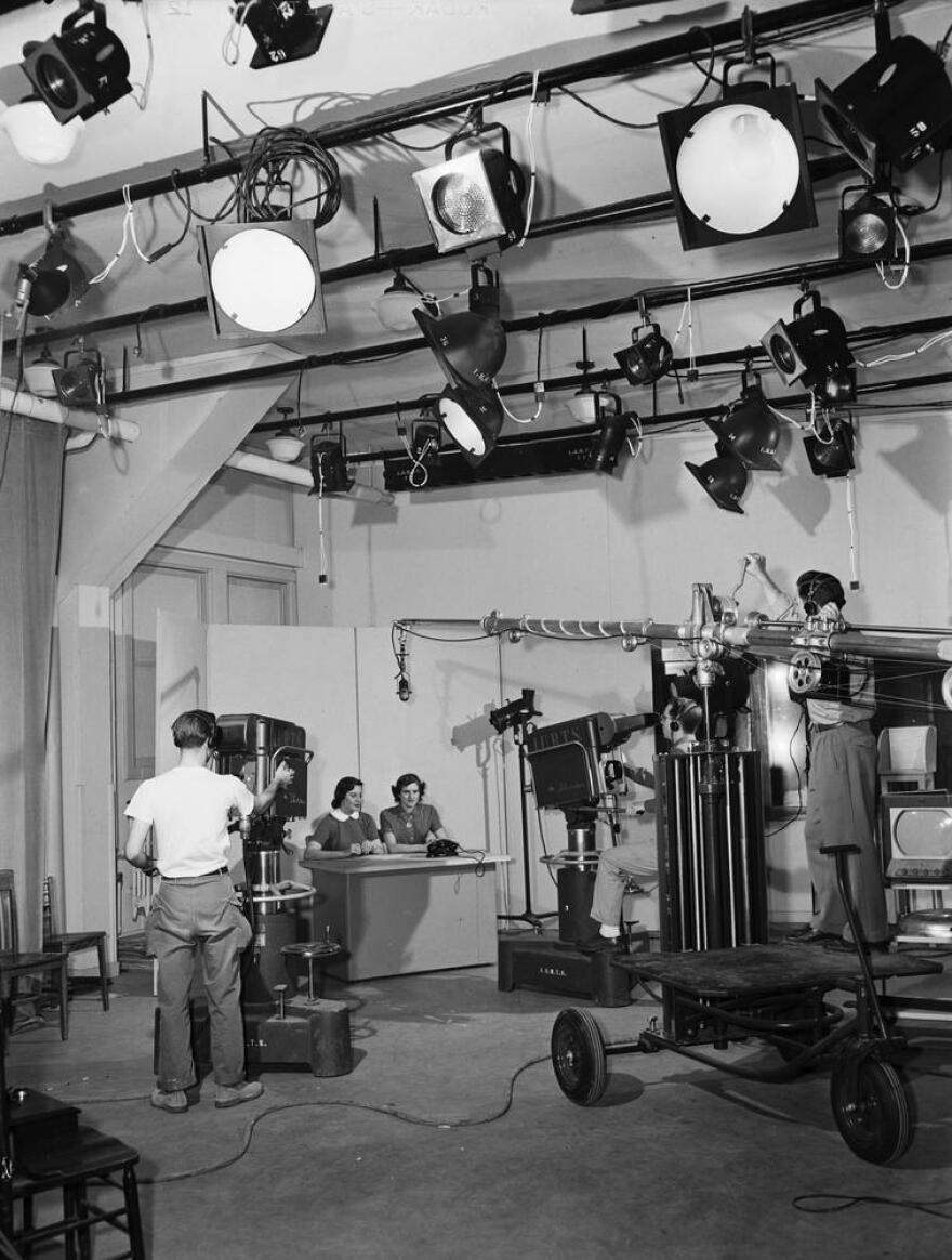 The RTV studio captured in nineteen-fifty-three in black and white. Lighting equipment is visible and a news desk.