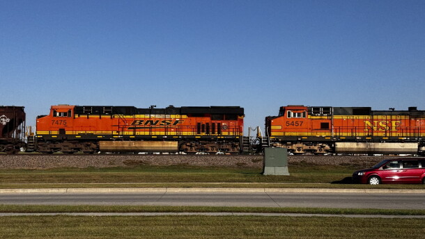Two orange train cars with the BNSF and NSF logos ride along the train tracks on the side of a road.