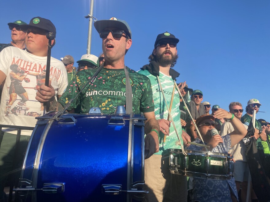 Two men wearing hats and sunglasses play drums at a Vermont Green soccer match