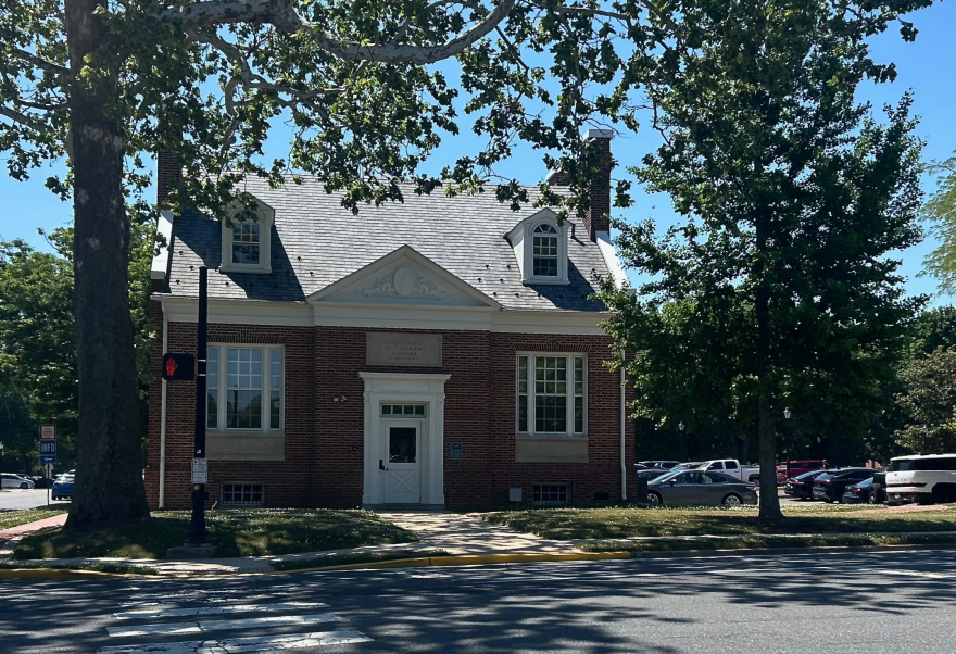 A brick building lined by trees with parking lots filled with parked cars on either side