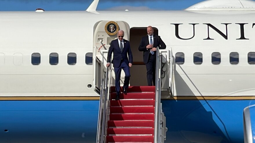 A mean in a suit and sunglasses walks down the stairs from an airplane. 