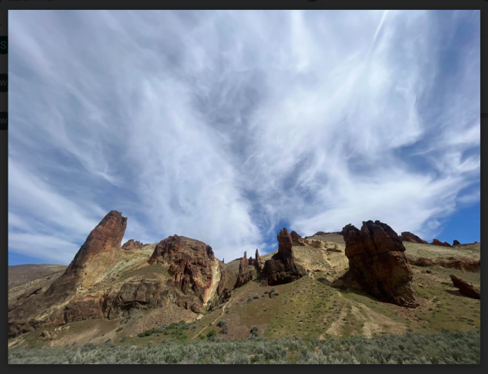Rocks jutting out of the green earth with blue sky and hazy white clouds above.