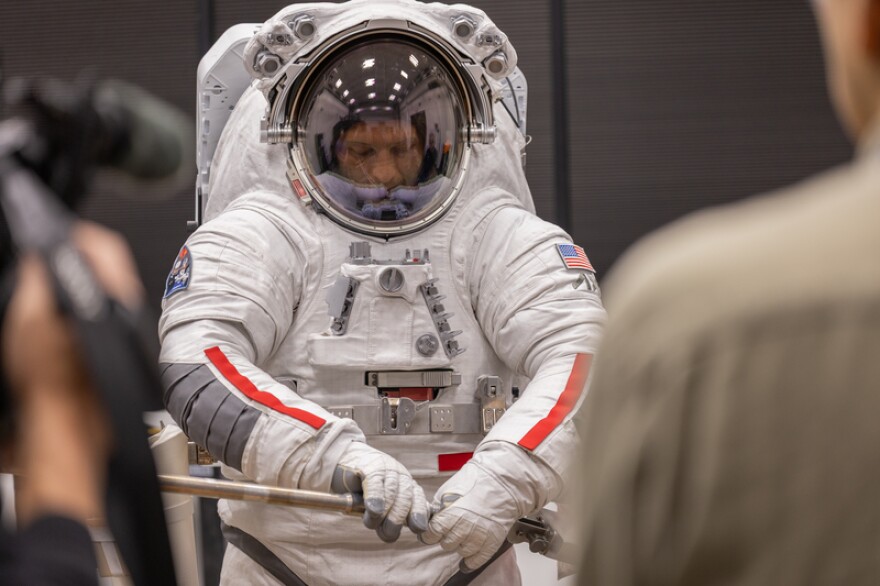 An Axiom Space engineer wearing the Axiom Extravehicular Unit (AxEMU) assembles a lunar sampling tool, demonstrating to visiting media what Artemis astronauts will do before collecting geological samples on the Moon.