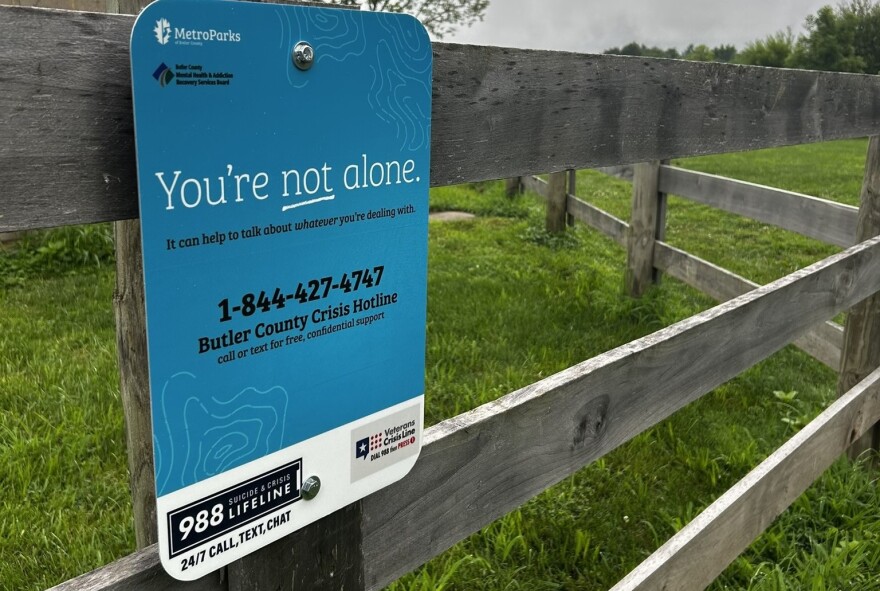 A blue sign listing phone numbers is attached to a wooden post and rail fence.